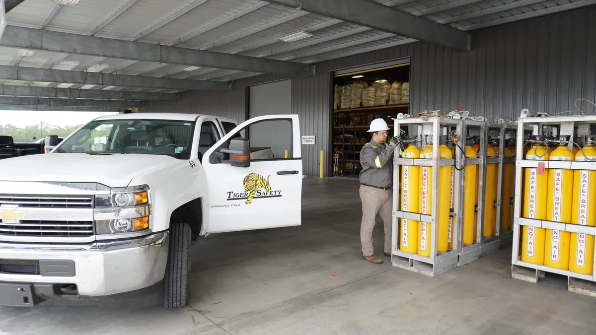 Tiger Safety technician checking breathing air cylinder racks beside a company truck